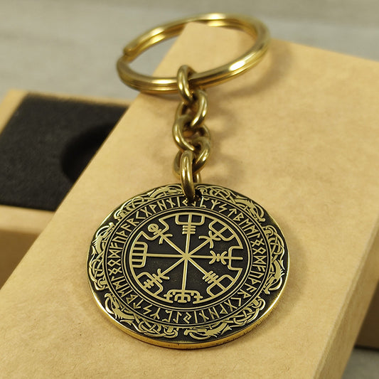 Close-up of a brass Vegvisir coin keychain with deep laser engraving, antique patina finish, and decorative border on a craft gift box.