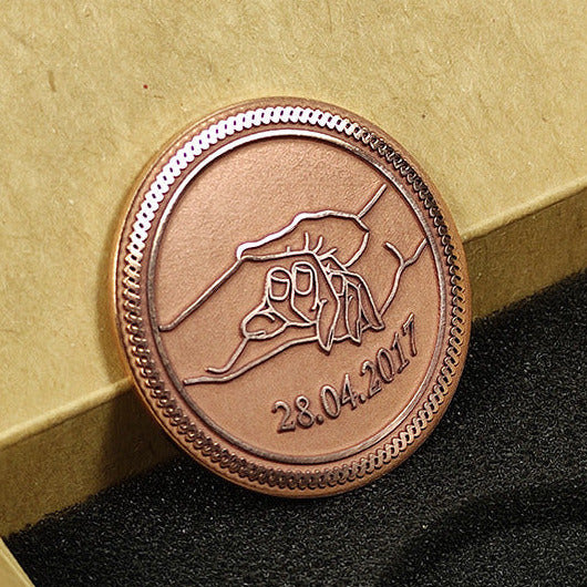 Close-up of a personalized copper coin featuring laser-engraved hands holding and a custom date, finished with dark antique patina.