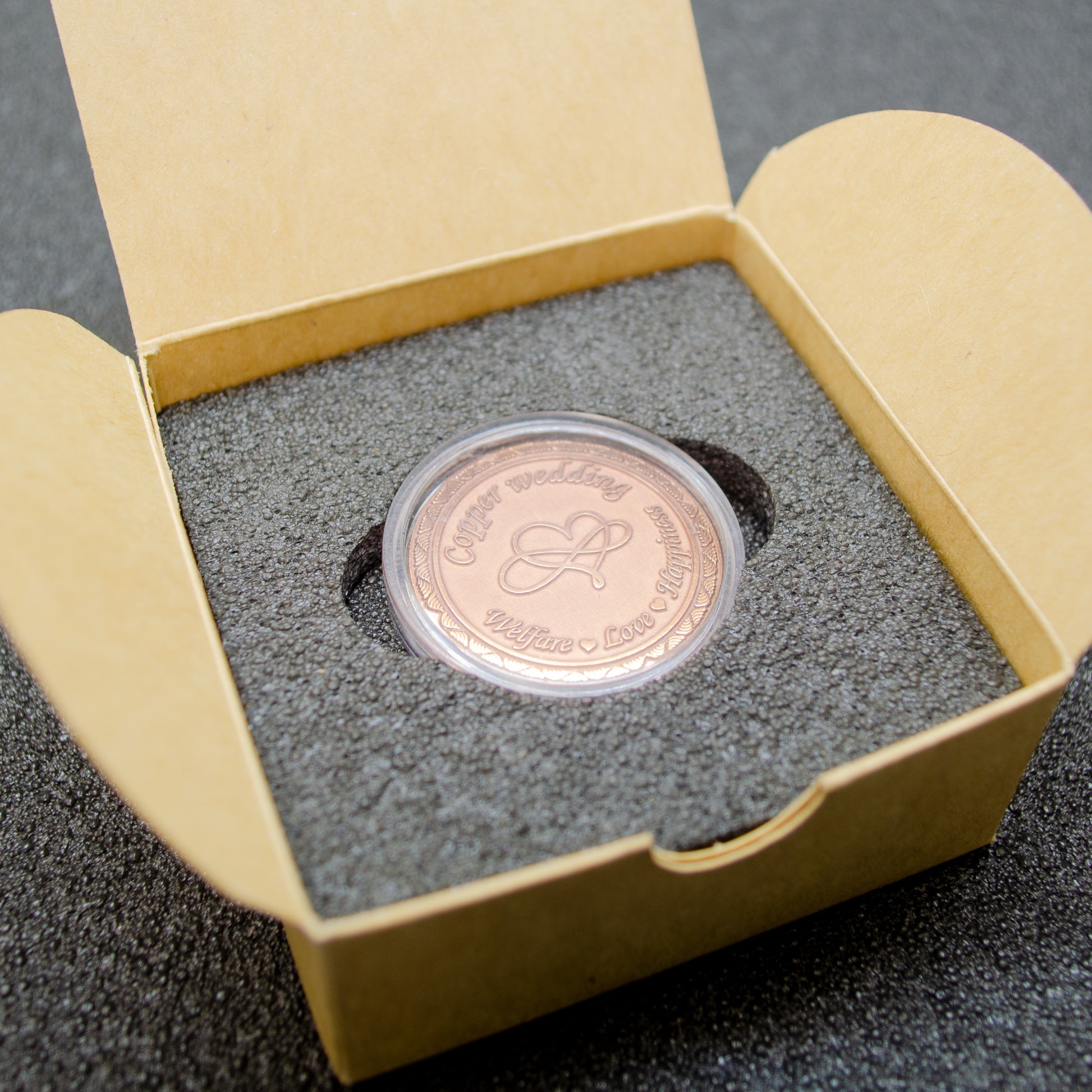 Top view of a personalized copper anniversary coin in a gift box, infinity heart custom engraved souvenir, premium gift presentation.