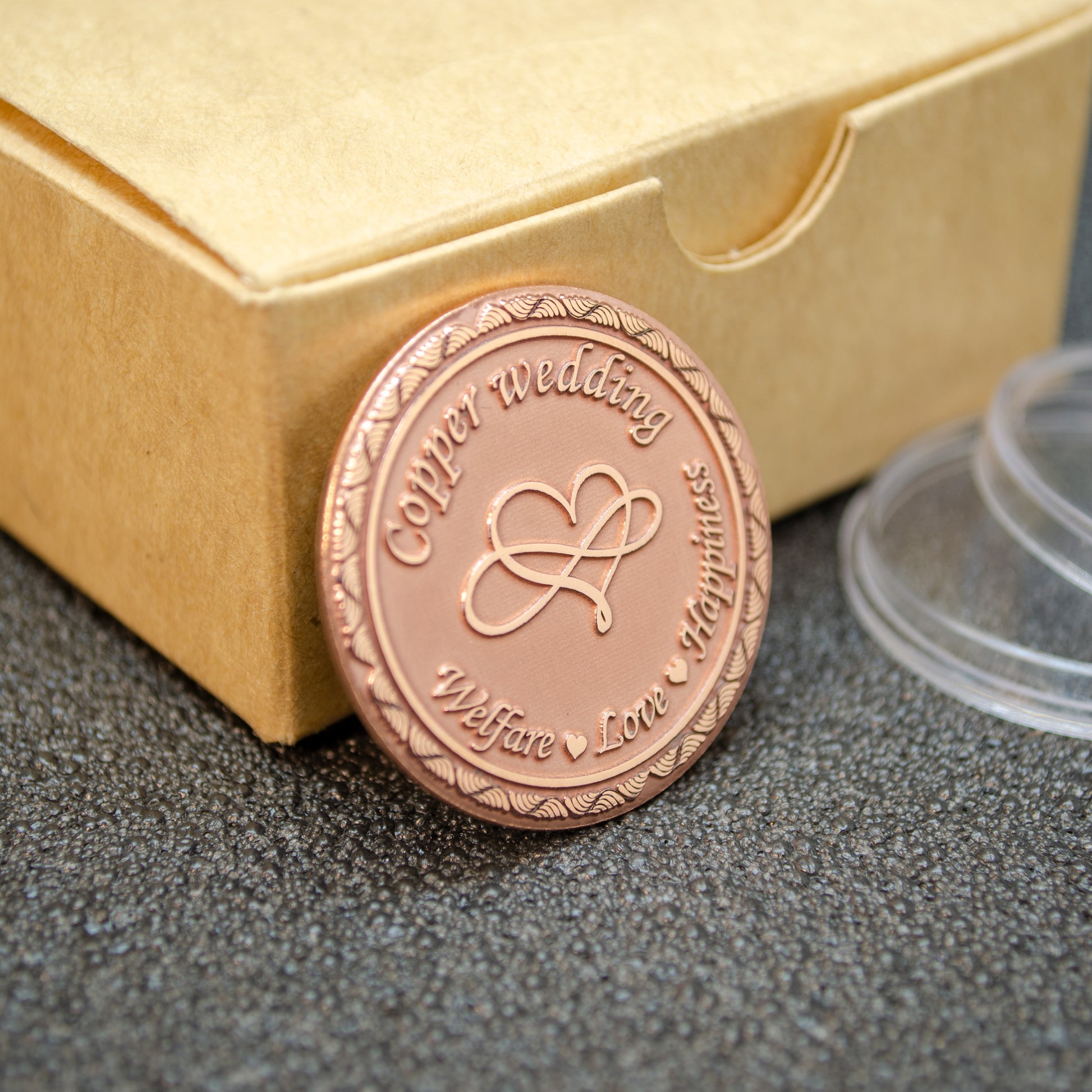 Customized copper anniversary gift, engraved "Welfare, Love, Happiness" token standing near craft box, polished copper metalwork.