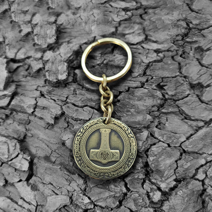 Personalized brass Thor's Hammer keychain on a rustic dark wood bark texture, highlighting the antique finish and durable metal quality of the talisman.