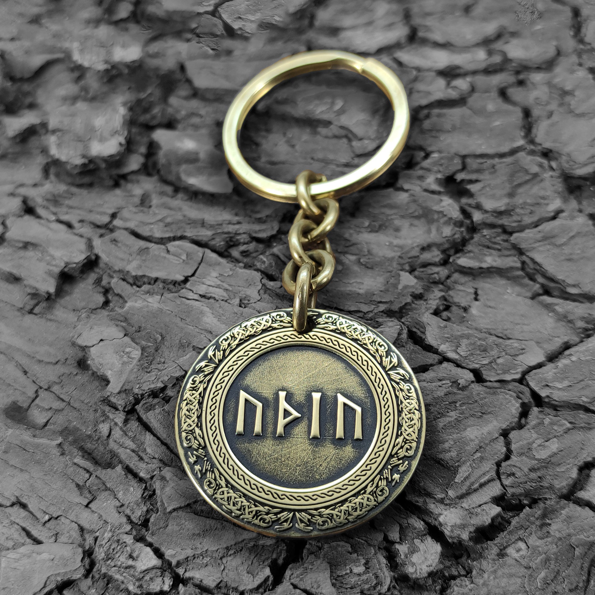 Brass rune keychain on a rustic dark wood bark texture, showcasing the antique finish and durable metal quality of the personalized talisman.