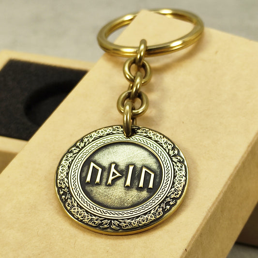 Close-up of a brass rune coin keychain with deep laser engraving, antique patina finish, and decorative border on a craft gift box.