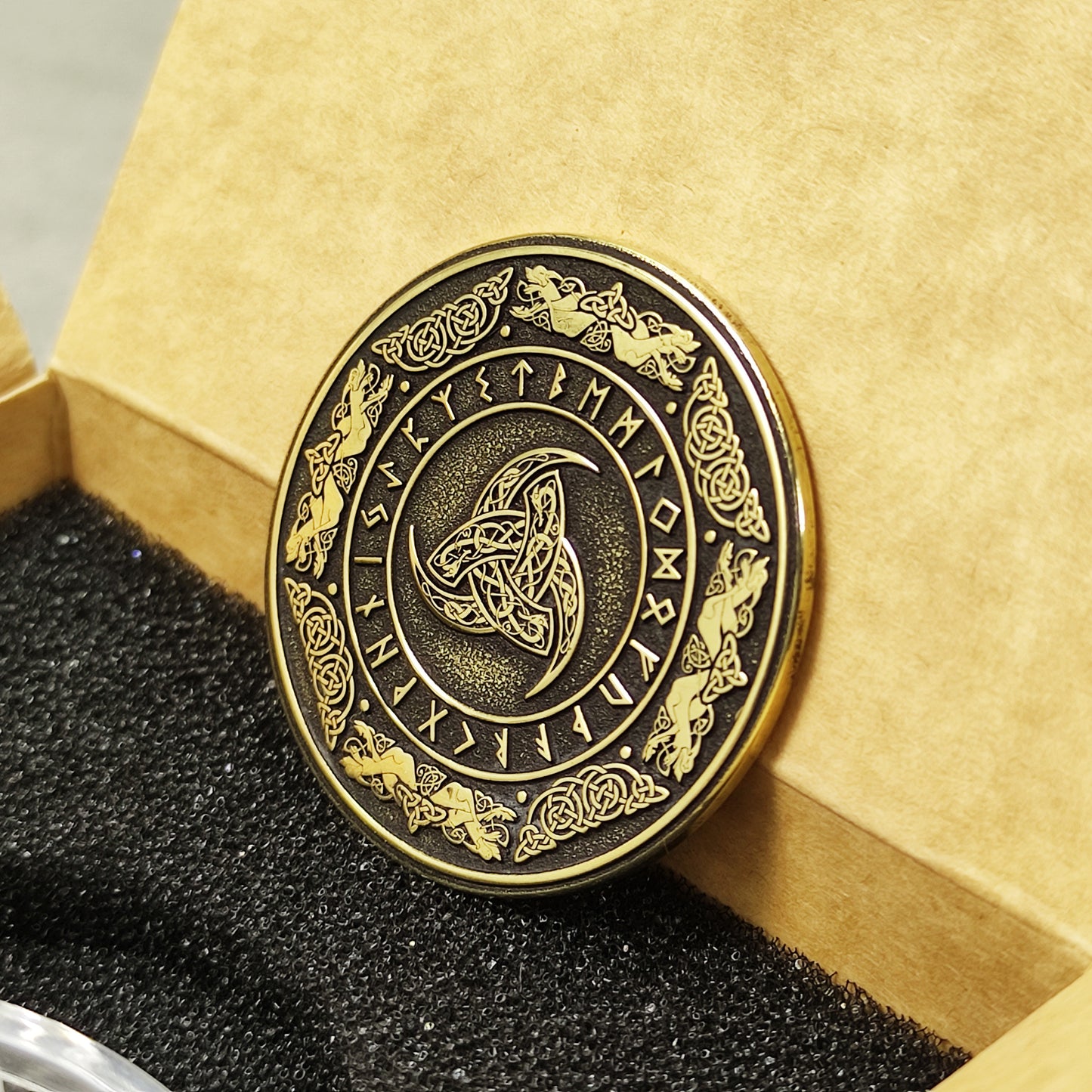 Perspective view of a 2mm thick brass challenge coin in a gift box, showcasing the metallic luster and detailed Viking symbolism.