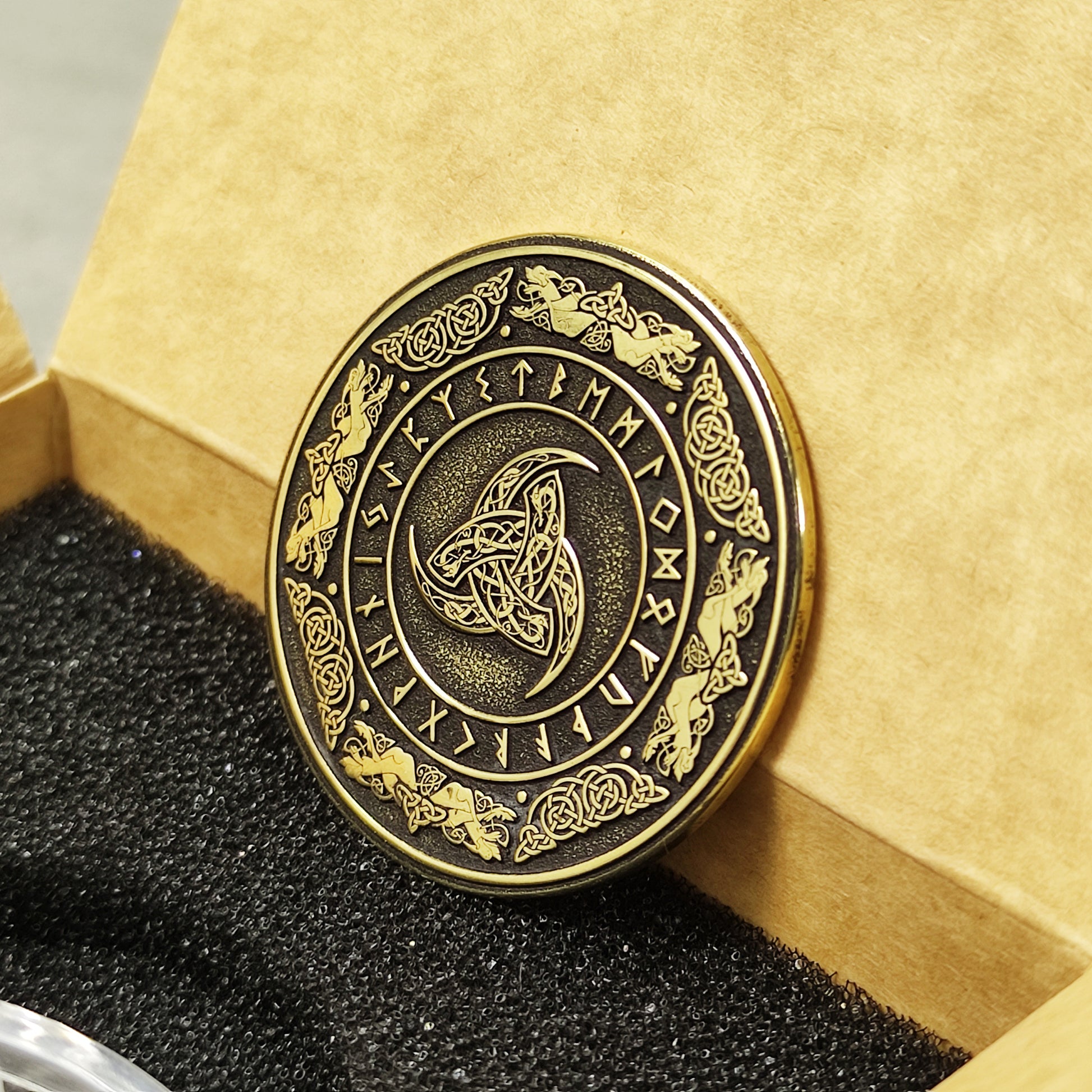 Perspective view of a 2mm thick brass challenge coin in a gift box, showcasing the metallic luster and detailed Viking symbolism.