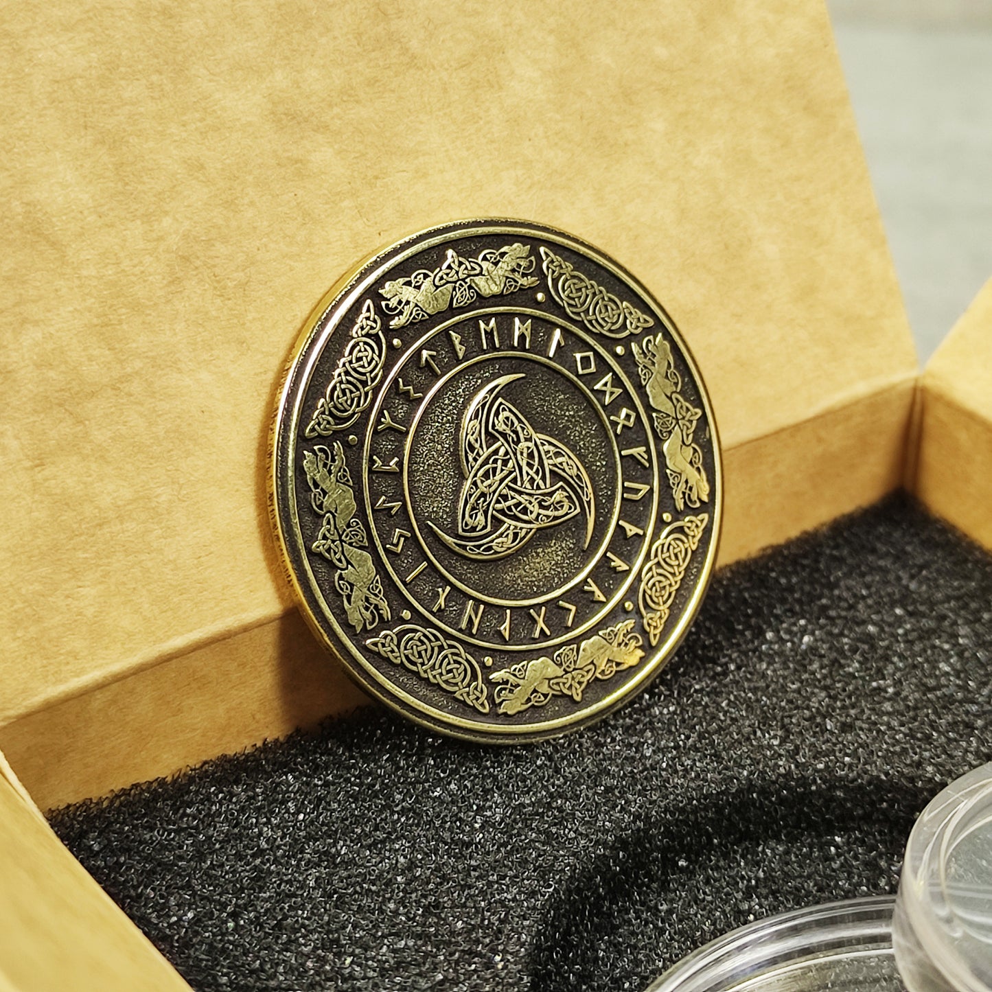 Vertical view of a handcrafted brass Odin's Horn coin, showing the golden texture and deeply etched Norse runes on a dark background.