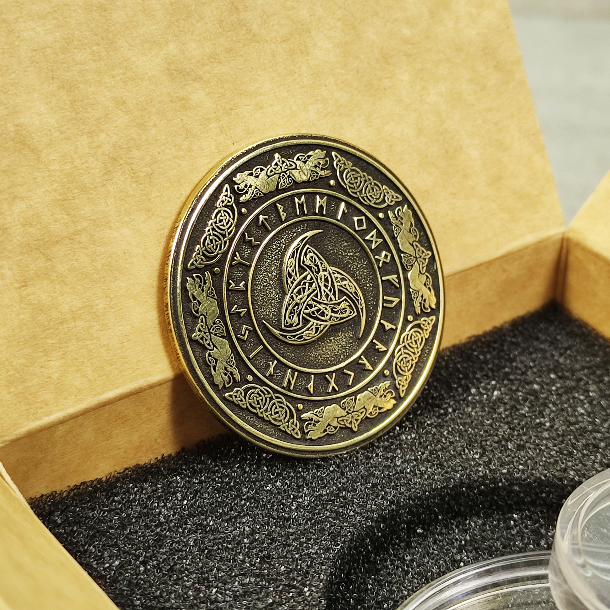 Vertical view of a handcrafted brass Odin's Horn coin, showing the golden texture and deeply etched Norse runes on a dark background.