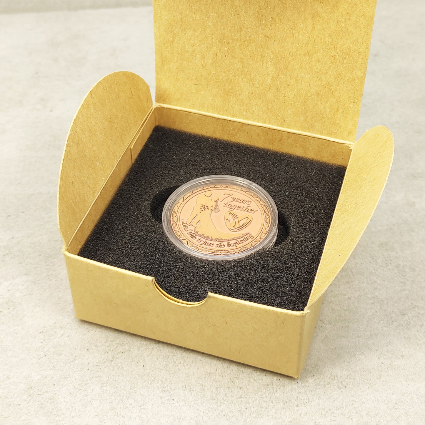 Top view of a personalized copper anniversary coin in a gift box, "7 years together" custom engraved souvenir, premium gift presentation.
