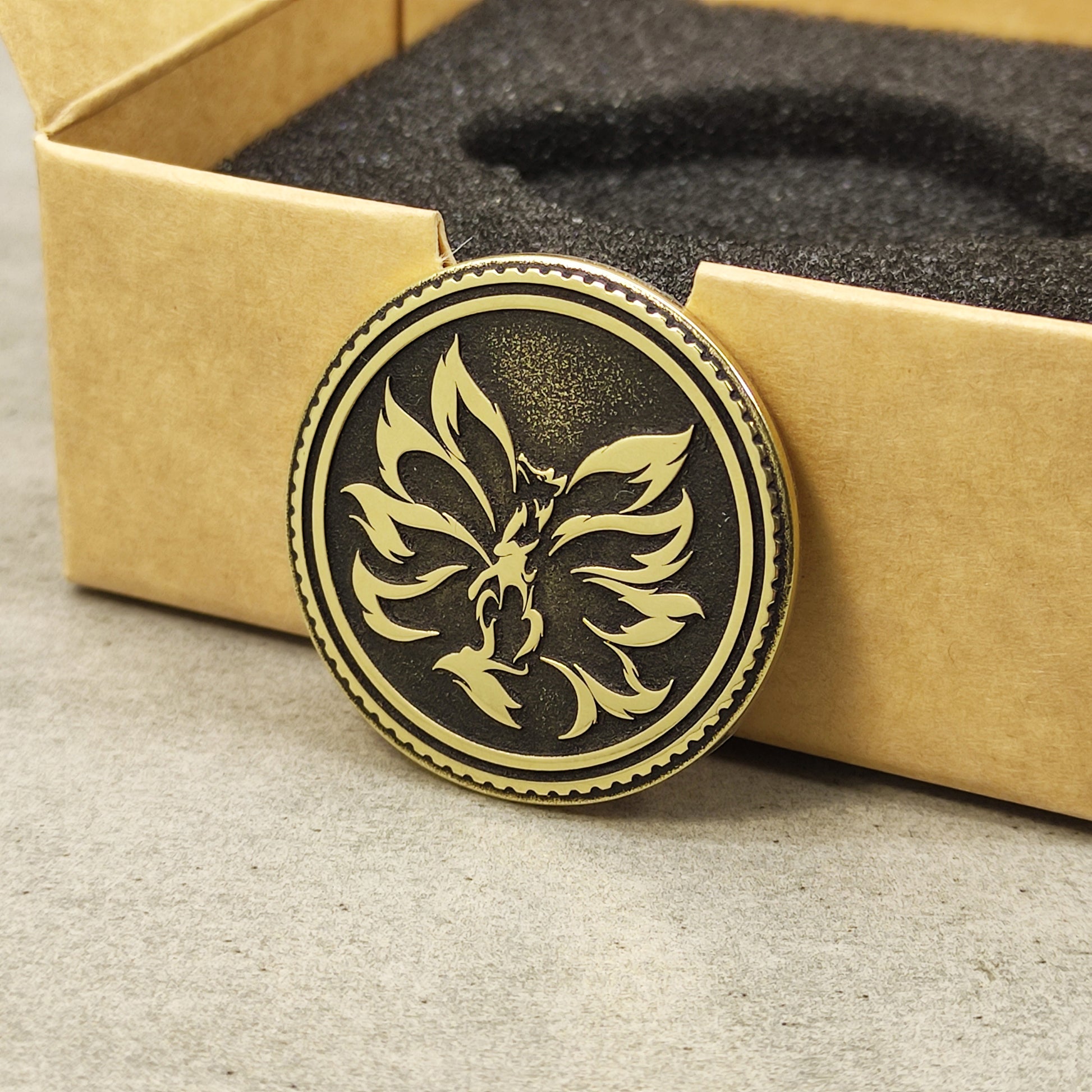 Vertical side-by-side view of a brass Kitsune coin and its eco-friendly gift box packaging with black foam insert.