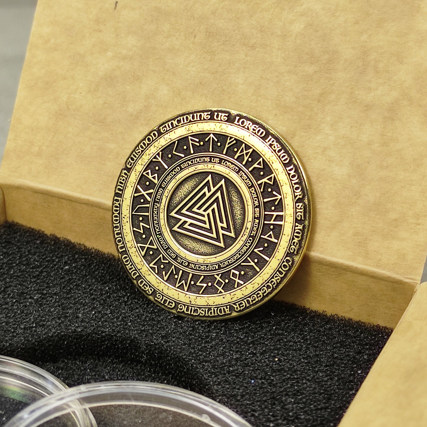 Vertical view of a handcrafted brass Viking coin, showing the golden luster and deeply etched Norse symbols on the surface.