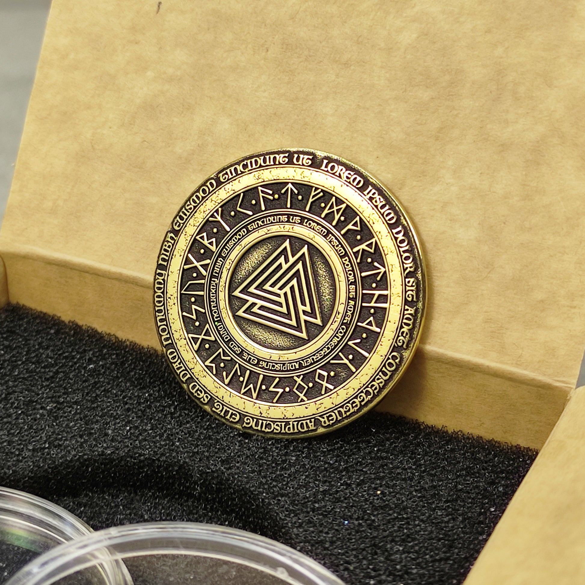 Vertical view of a handcrafted brass Viking coin, showing the golden luster and deeply etched Norse symbols on the surface.