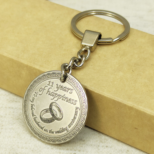 Close-up of 11th wedding anniversary brass coin keychain for husband, features deep laser engraving of intertwined wedding rings and personalized text with dark patina.