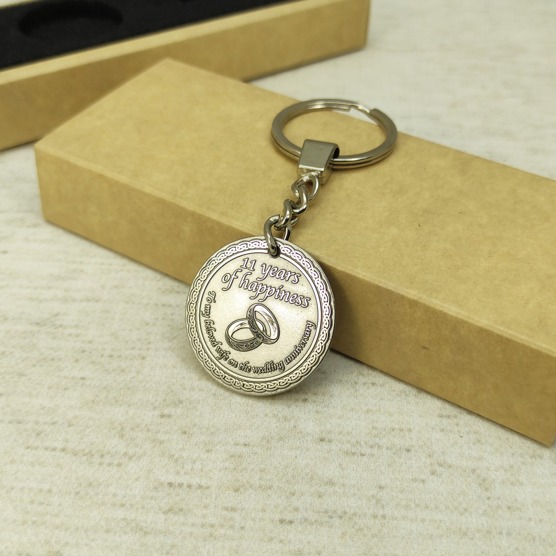 Top view of 11th wedding anniversary brass coin keychain placed next to craft gift packaging, personalized engraved metal souvenir for wife.