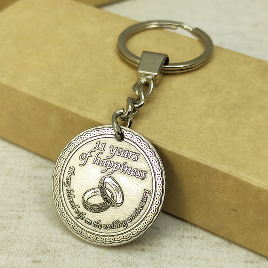 Close-up of 11th wedding anniversary brass coin keychain for wife, features deep laser engraving of wedding rings and personalized text with dark patina finish.