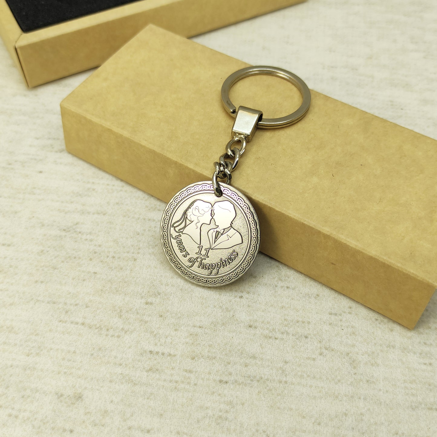 Personalized 11th anniversary steel keychain on a minimalist gift packaging background, elegant custom engraved metal keepsake for spouse.