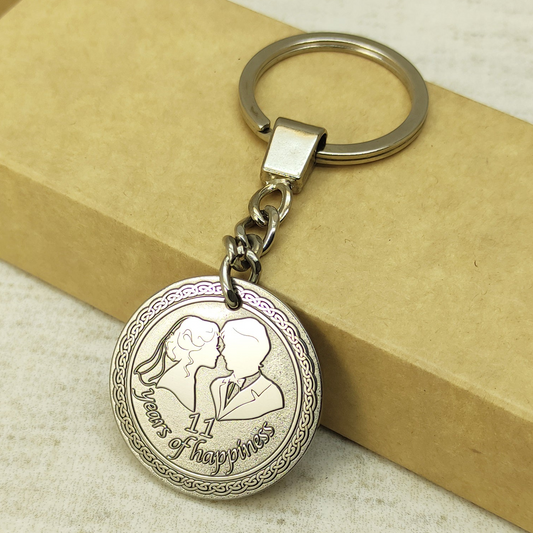 Close-up of stainless steel 11th wedding anniversary keychain with personalized engraving of a couple and "11 years of happiness" text, high-quality deep laser etching on metal coin.