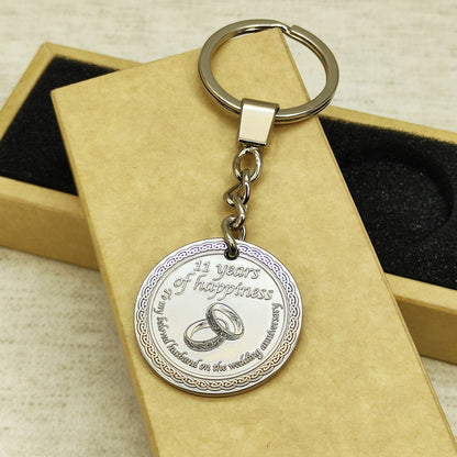 11th wedding anniversary brass coin keychain on craft gift box background, personalized metal souvenir for husband with custom laser engraved symbolic rings.