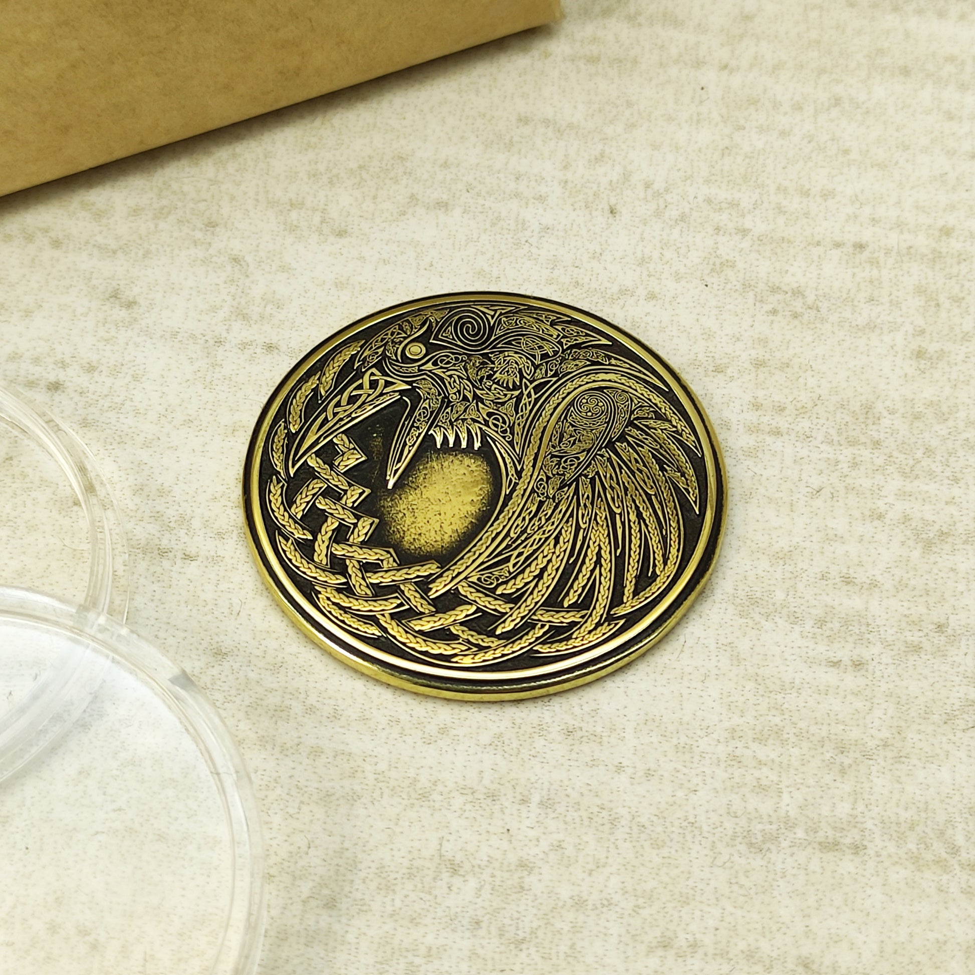 Top view of a brass Norse Raven amulet coin, detailed Scandinavian knotwork engraving with high-contrast antique finish.