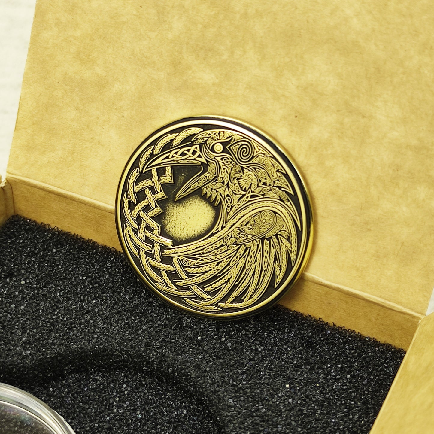 Vertical view of a handcrafted brass Odin's Raven coin, highlighting the golden texture and deeply engraved Norse symbolism.