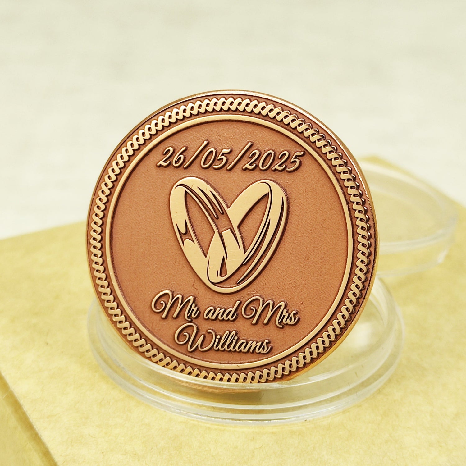 Close-up of a personalized copper wedding coin featuring custom laser engraved names, date, and intertwined rings on a matte metallic surface.