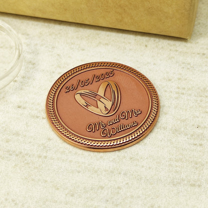 Top view of a personalized copper coin for couples, highlighting the intricate details of the engraved wedding rings and decorative border.