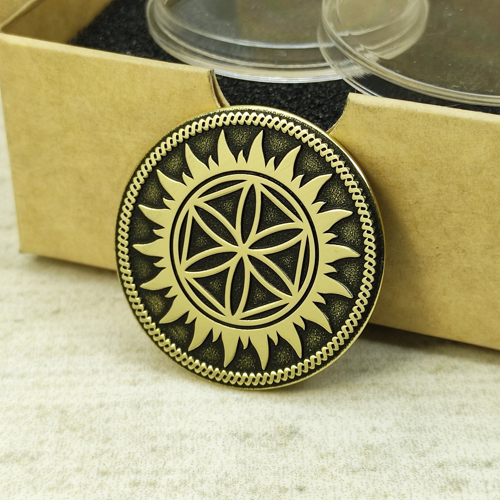 Vertical view of brass Perun Star protective coin showing thick edge and deep relief engraving next to a gift box.