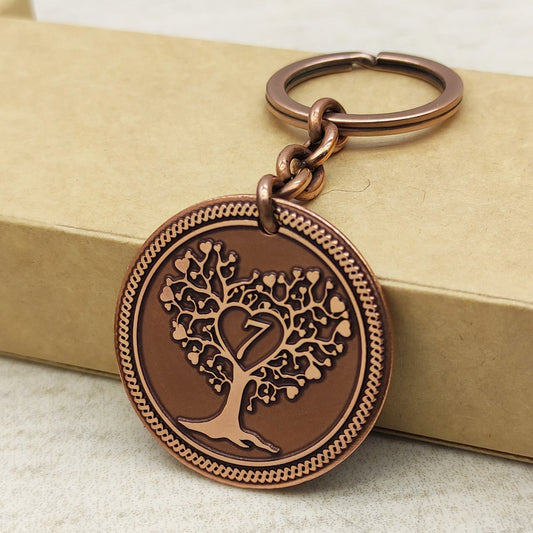Close-up of 7th anniversary copper coin keychain with Tree of Life engraving and dark patina finish against a craft box.
