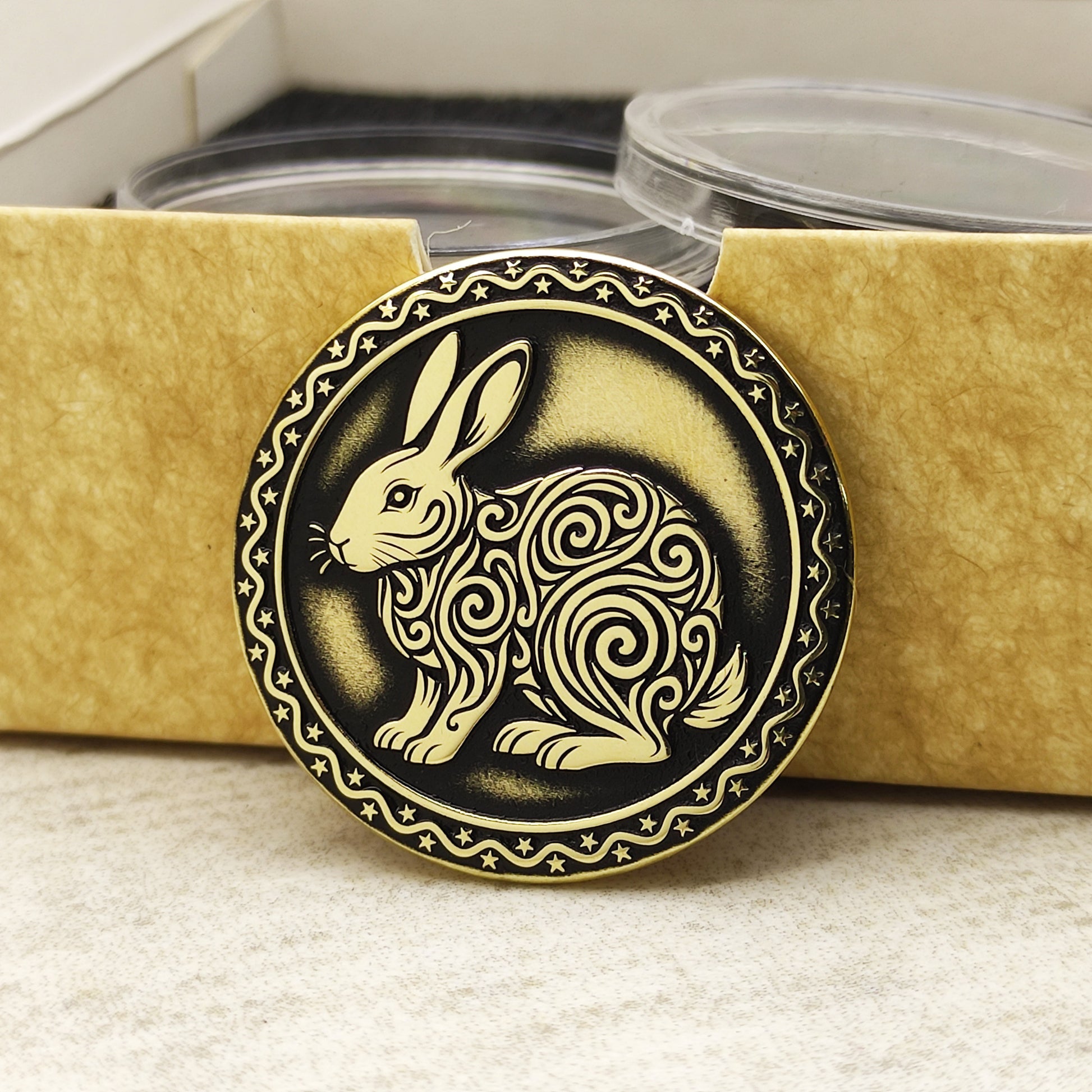 Brass Year of the Rabbit zodiac coin leaning against an eco-friendly craft gift box, highlighting the polished brass quality and ornamental edge.
